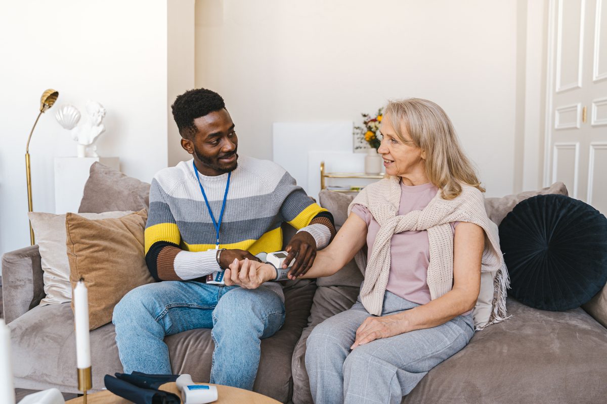 A caregiver checking an older woman's blood pressure at home